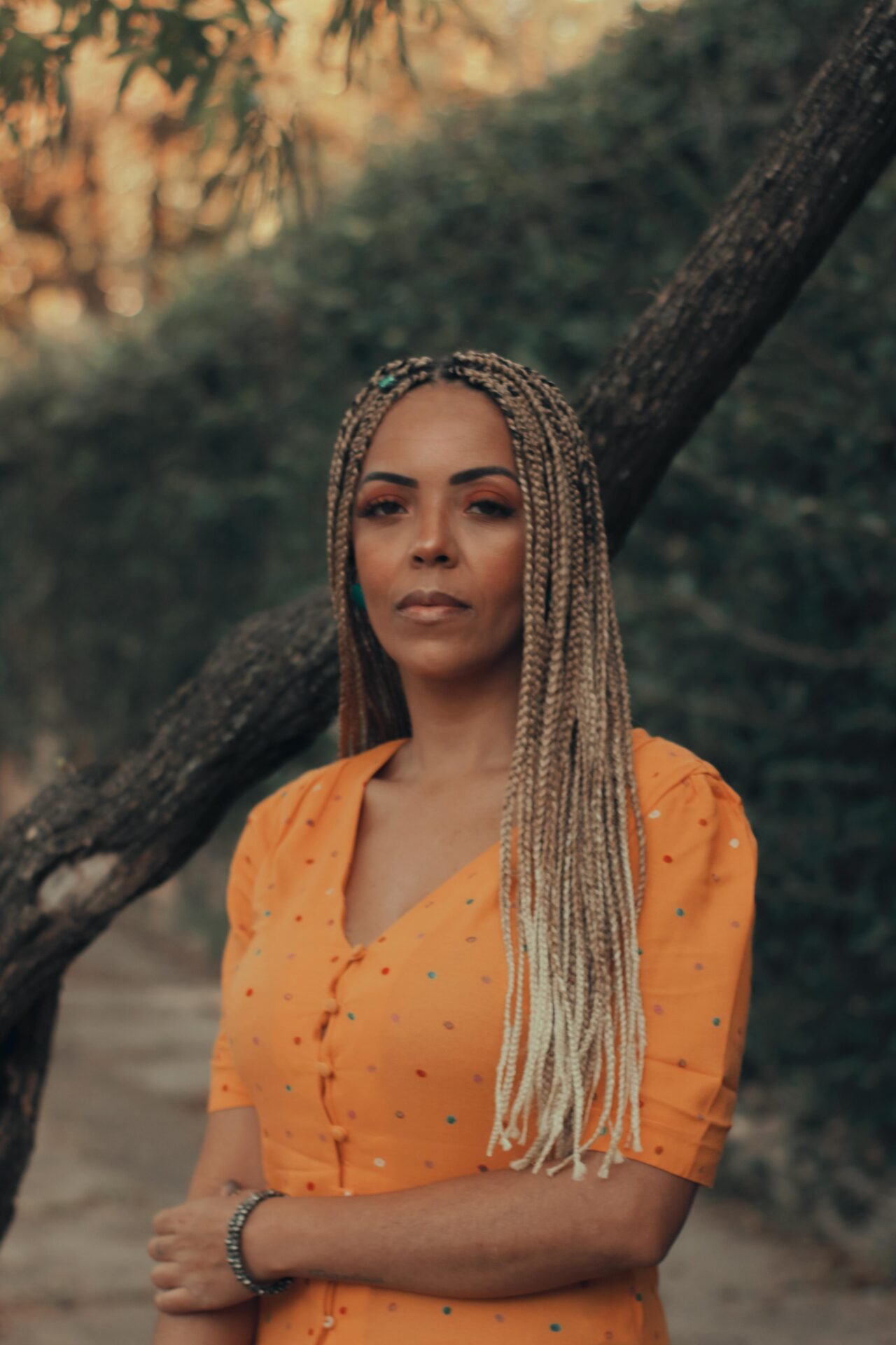 Elegant woman in yellow dress with braids poses outdoors, capturing a serene moment.