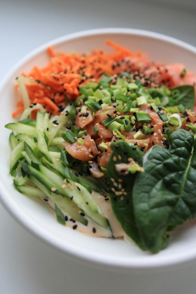 A vibrant salmon salad with cucumbers, carrots, and sesame seeds in a white bowl.